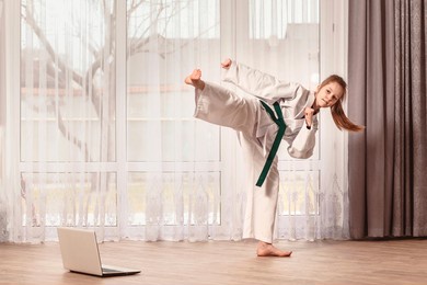 little girl doing homework with taekwondo. the child trains at home in front of a laptop.