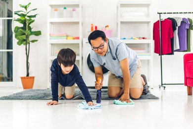 father teaching asian kid little boy son use disinfectant spray bottle cleaning and washing floor wiping dust with rags while cleaning house together at home