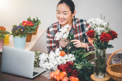 teaching flower arrangements online in the house concept, asian woman smiling florist record video broadcast or course on smartphone or computer, compose arrange floral decorations,online flower shop.