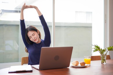 young asian woman is relaxing to stretching and eating bread with a glass of orange juice while break time after working hard at home