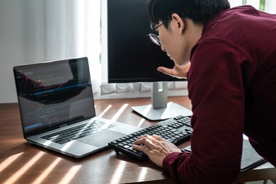 asian man programmer looking and touching on screen laptop to typing code data with keyboard about website or applications while working hard for new project in software development office