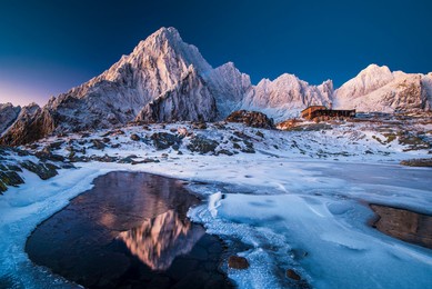 romantic mountain hut in a snowy valley in the middle of the mountains with majestic mountains reflected on the lake surface. lake with ice structures. high tatras, slovakia