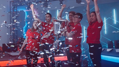 diverse esport team winner of the video games tournament celebrates victory cheering and lifting trophy in big championship arena. cyber gaming event with gamers and fans.