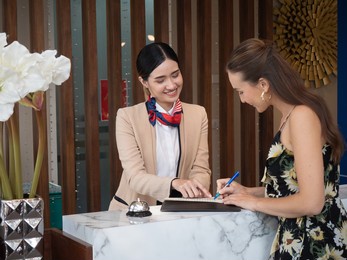 young travelers talking and check-in register information with woman receptionist worker standing in counter hotel reception counter desk at lobby modern hotel.