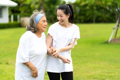 asian senior mother and adult daughter holding hands and exercise walking outdoor at  park. 