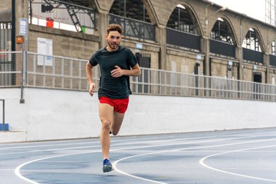 young runner man wearing sports clothes running in track and field.