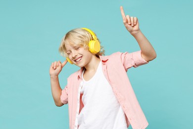 funny little curly kid boy 10s years old in casual pink shirt listening music with headphones dancing isolated on blue turquoise color background children studio portrait. childhood lifestyle concept