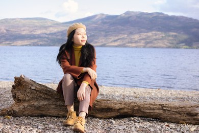 young asian woman with fall,  autumn, and spring fashion wear sitting down on a log by a lake	