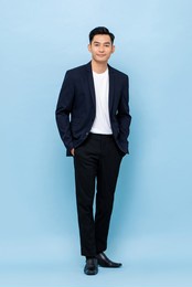 full length portrait of happy smiling young handsome southeast asian businessman standing on light blue studio background