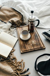 open book in bed with coffee brewed in a french press and cup on a wooden board. morning at home, coziness and comfort.