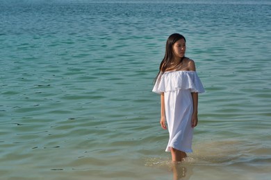 young asian pregnant woman in a white sundress in the water by the sea