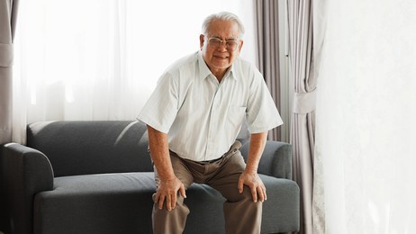 knee problem of senior, has leg pain when standing up and sitting down during old age. asian senior has knee pain after stand up and sit down in living room at home.