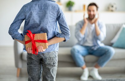 father's birthday. boy preparing surprise for dad holding wrapped gift box behind back. son congratulating daddy on his b-day at home. family holiday concept. selective focus on present