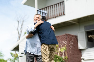 senior asian father with adult grown son hugging outdoors.