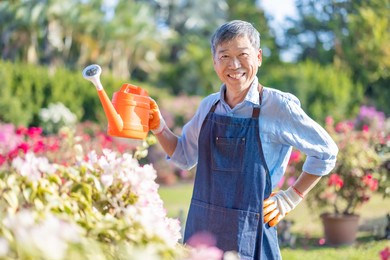 authentic shot of asian retired senior man watering plants in the garden - smiling at you