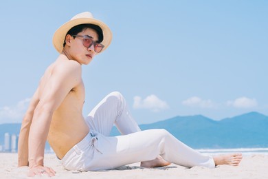 barebacked young asian man sitting on the sand and looking at the sea
