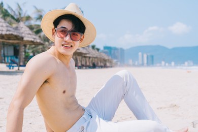 barebacked young asian man sitting on the sand and looking at the sea
