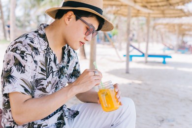 young asian man drinking orange juice on the beach
