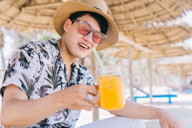 young asian man drinking orange juice on the beach
