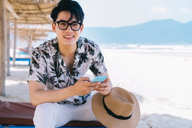 young asian man using smartphone on the beach