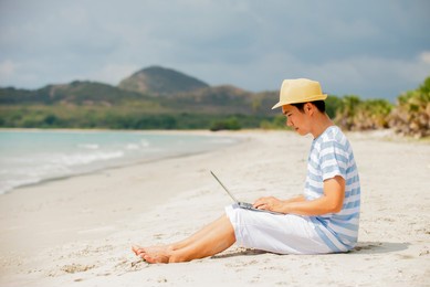 asian man  sitting on sand at beach using laptop computer working , freelance working distancing , e-learning , travel summer holiday business technology  online concept