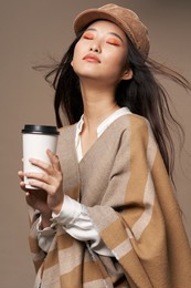 asian woman with cup of coffee and in fashionable clothes on beige background cropped view