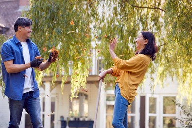 mature asian couple having fun throwing leaves as they working in garden at home together