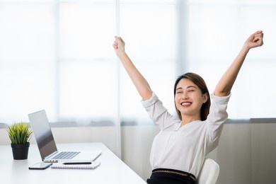 young beautiful asian business woman finish working and celebrate with two hand stretch in the air. women finished work and rest she works at home in the living room.