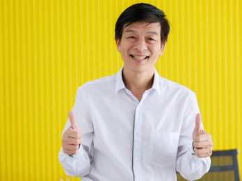 portrait of senior middle aged businessman in white shirt standing and give two thumbs up with self-confidence in office