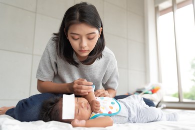 sick asian baby lying on the bed with a cool jell at head for reducing temperature.
