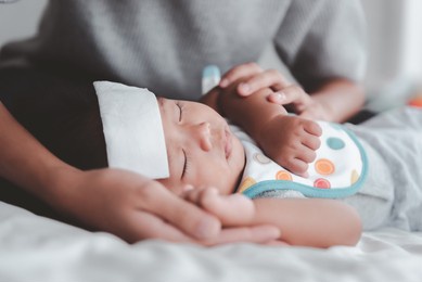 sick asian baby lying on the bed with a cool jell at head for reducing temperature.