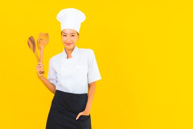 portrait beautiful young asian chef woman with spatula on yellow isolated background