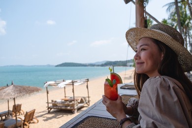 a beautiful young asian woman drinking watermelon juice while sitting in the beach cafe