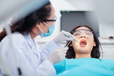 dentist using dental mirror and tweezers when checking teeth of young female patient