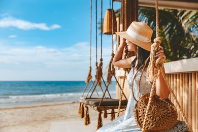 travel summer vacation concept, happy traveler asian woman with hat and dress relax on swing in beach cafe, koh chang, thailand
