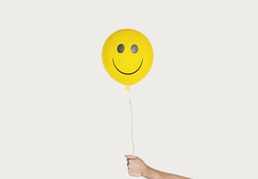 hand holding smiling face yellow balloon, isolated on white background