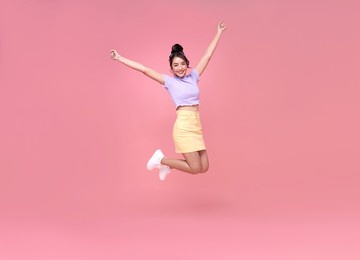 happy asian woman smiling and jumping while celebrating success isolated over pink background.