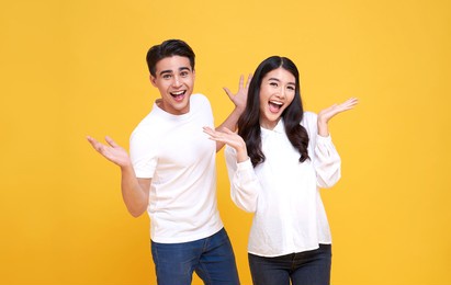 smiling young asian couple man and woman happy and amazed on yellow background.