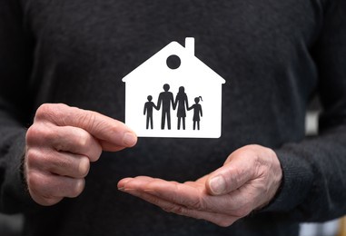 man holding a paper house and family; concept of family and house insurance
