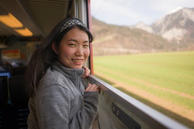 train travel getaway - young happy and beautiful asian korean woman enjoying snow landscape through railcar window during winter holiday trip
