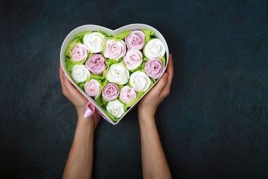 marshmallow roses in a gift box in the shape of a heart on a dark gray background. a sweet gift for a girlfriend or mom. hands are holding a gift box. view from above. copy space.