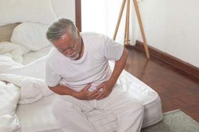 asian elderly man stomachache in bedroom.