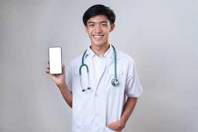 handsome young asian doctor man smiling showing blank phone screen display for a copy space, isolated on white background