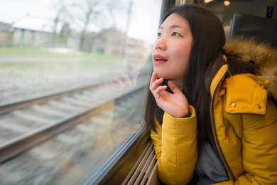 young beautiful and happy asian japanese woman sitting on train looking out to window enjoying holidays travel in europe smiling thoughtful and sweet
