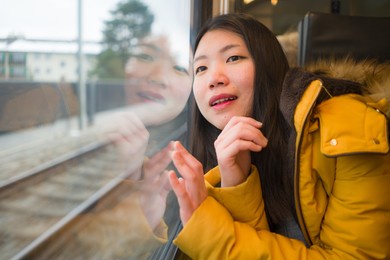 young beautiful and happy asian chinese woman sitting on train looking out to window enjoying holidays travel in europe smiling thoughtful and sweet