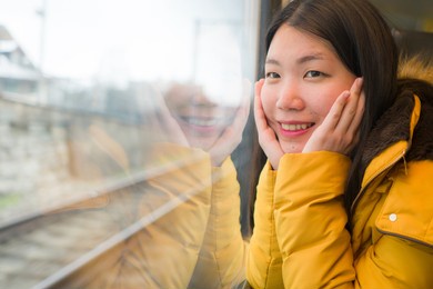 young beautiful and happy asian chinese woman sitting on train looking out to window enjoying holidays travel in europe smiling thoughtful and sweet