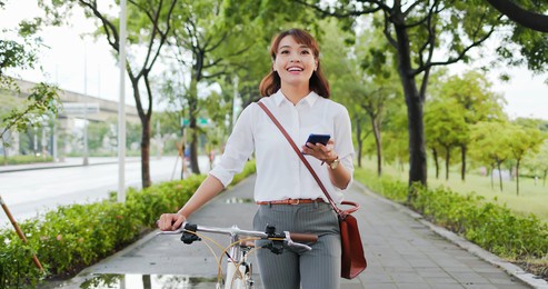 asian businesswoman commute with her bicycle and use phone in the streets happily
