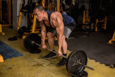 a large and muscular asian man does block deadlifts. barbell elevated from floor with steel plates. working out at a hardcore gym.