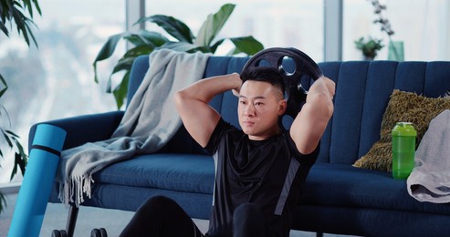 handsome strong asian young man engaged in heavy sports bodybuilding lifting barbell disc practicing strength endurance working out in living room.