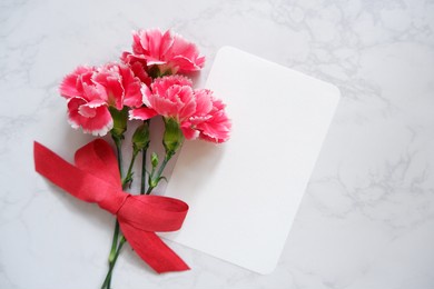 a blank greeting card with carnation flowers and red ribbon on white marble background. mother’s day, father’s day, weeding celebration background.